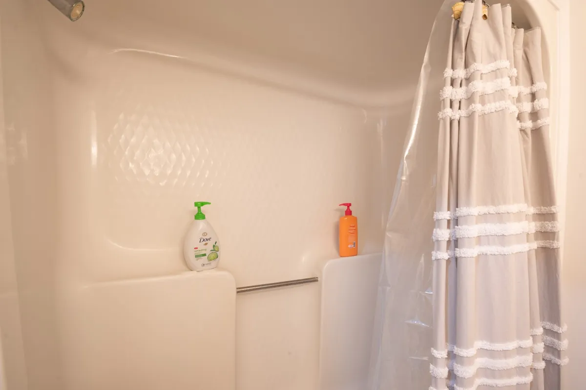 This interior image spotlights a shower area with a clean shower curtain, wall, and convenient soap dispensers. The mood is refreshing, evoking the idea of rinsing off after a beach day, which aligns perfectly with the section’s mention of an outdoor sand shower.