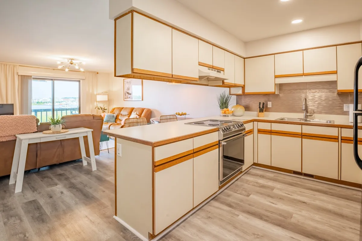 A bright, updated interior featuring a stylish kitchen countertop with modern stainless steel appliances and a comfortable living area seating arrangement. The scene conveys a welcoming, cozy space ideal for gathering after a day out.