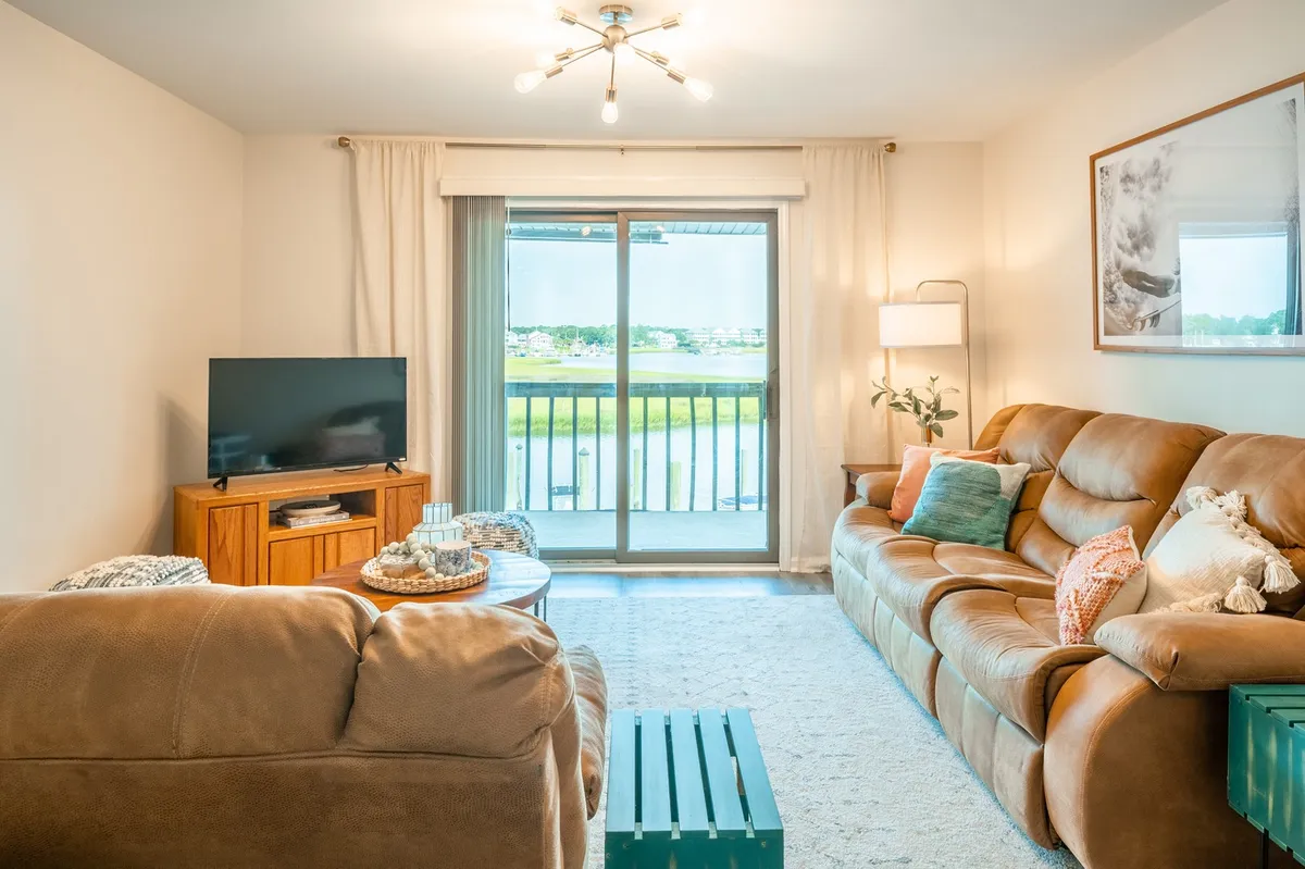 A cozy living room with a comfortable brown couch, wooden coffee table, and a large sliding glass door that opens to a stunning water view. Decorative pillows add warmth, while the proximity to the balcony enhances the seamless connection between indoor comfort and outdoor beauty.