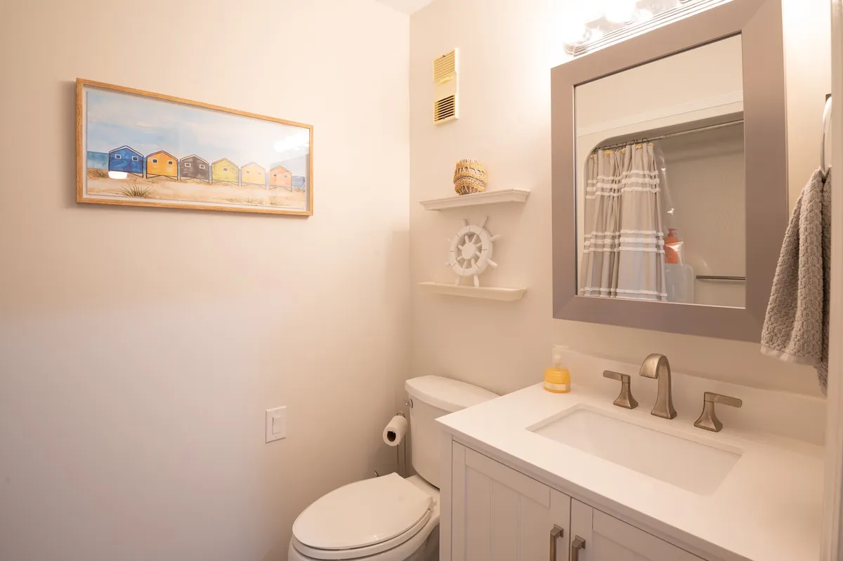 A bright bathroom with a stylish sink and faucet, neatly arranged shelves, and a framed painting of beach houses providing cheerful decor. The space feels calm and spa-like, ideal for relaxation and morning routines.