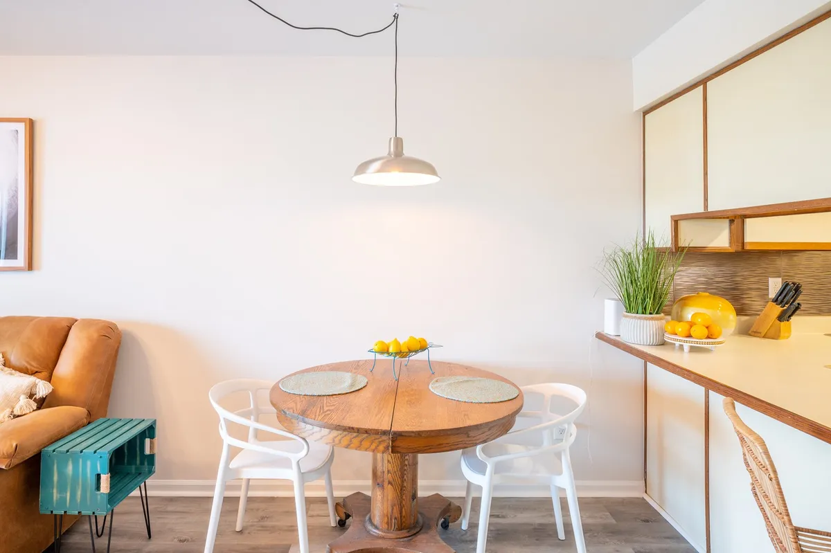 The scene centers on an antique wooden dining table surrounded by white chairs and a brown armchair. A decorative bowl of lemons adds freshness to the space, which is set for casual dining and social gatherings. The composition suggests warmth and intimacy—perfect for shared meals and cozy conversations.